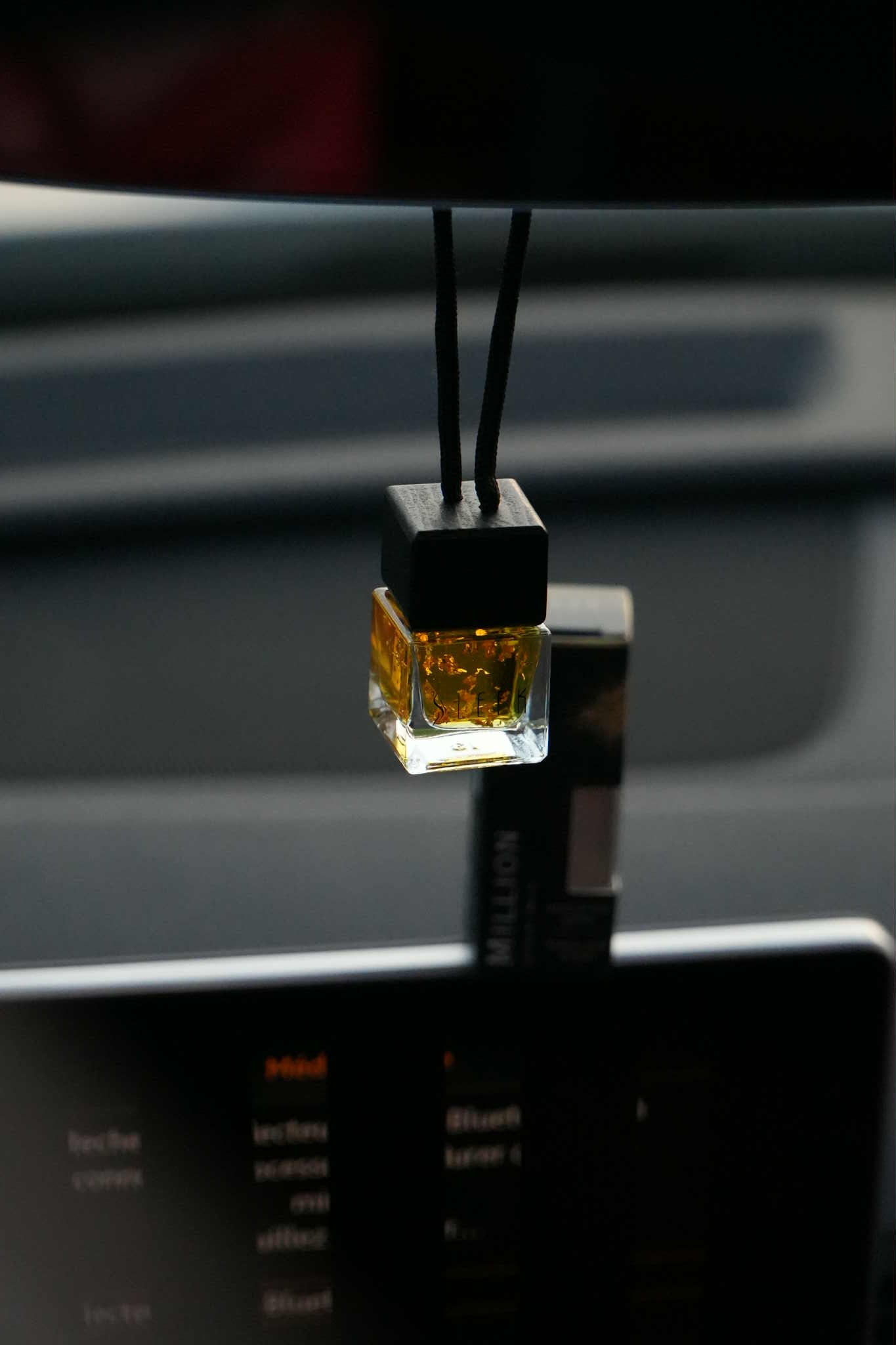 Car air freshener hanging from a car's rearview mirror with a blurred interior background.